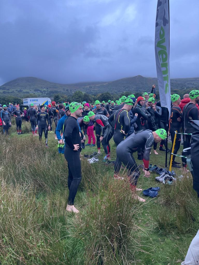Image of male athlete in wetsuit surrounded by other athletes before a swim event.