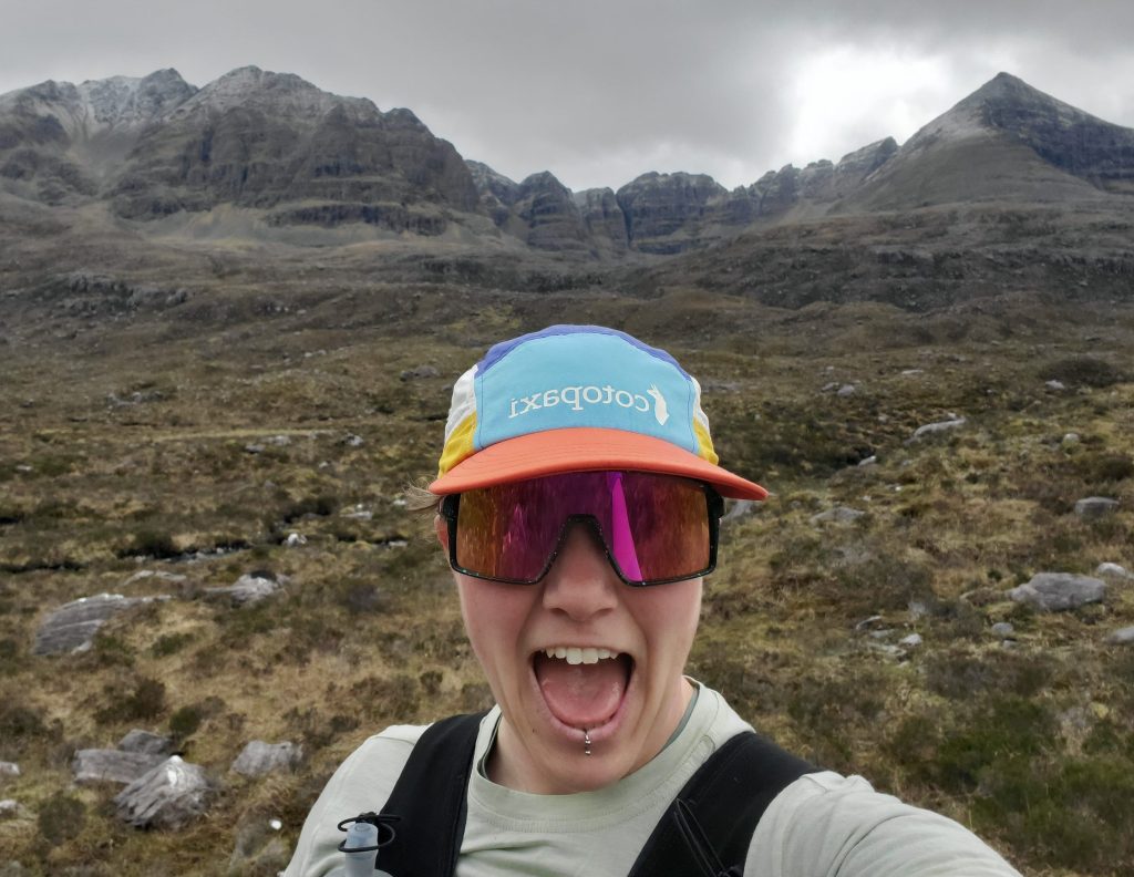 image of lady wearing sports cap and sunglasses surrounded by mountains